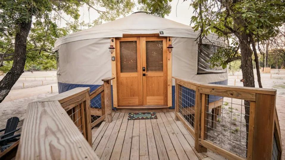 Blue Jay Yurt — wooden entry deck and double doors beneath mature live oaks.