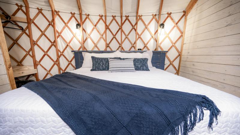 Blue Jay Yurt — king bed with navy linens beneath the exposed lattice wall.