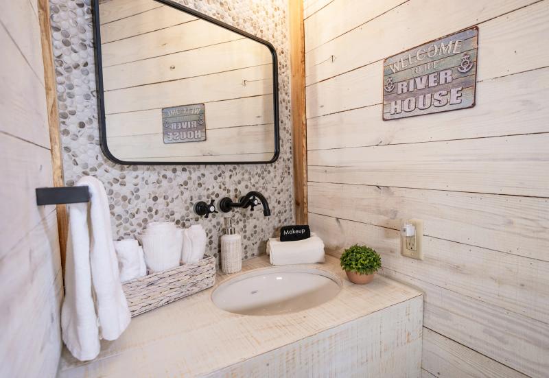 Blue Jay Yurt — whitewashed vanity with a pebble-tile backsplash and a painted “Welcome to the River House” sign.