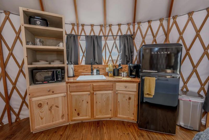 Canary Yurt — compact kitchen with wood cabinetry, refrigerator, and coffee station.