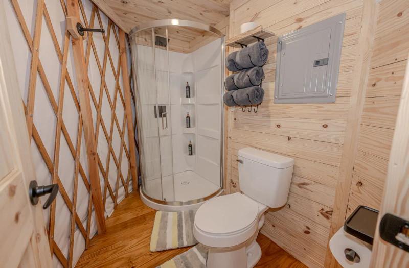 Canary Yurt — private bathroom with curved glass shower and stacked towels.