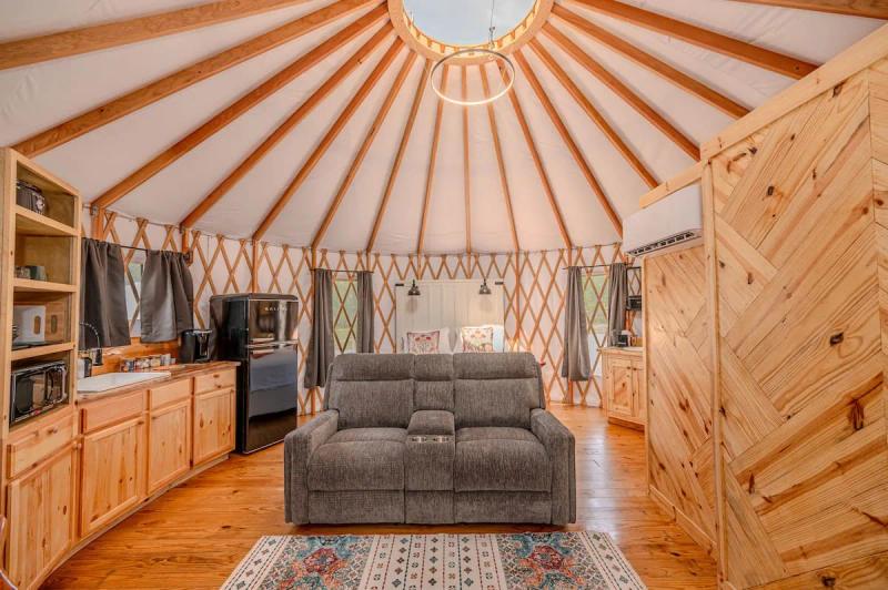 Cockatoo Yurt — wide interior with loveseat, kitchen, bed, and circular roof beams.