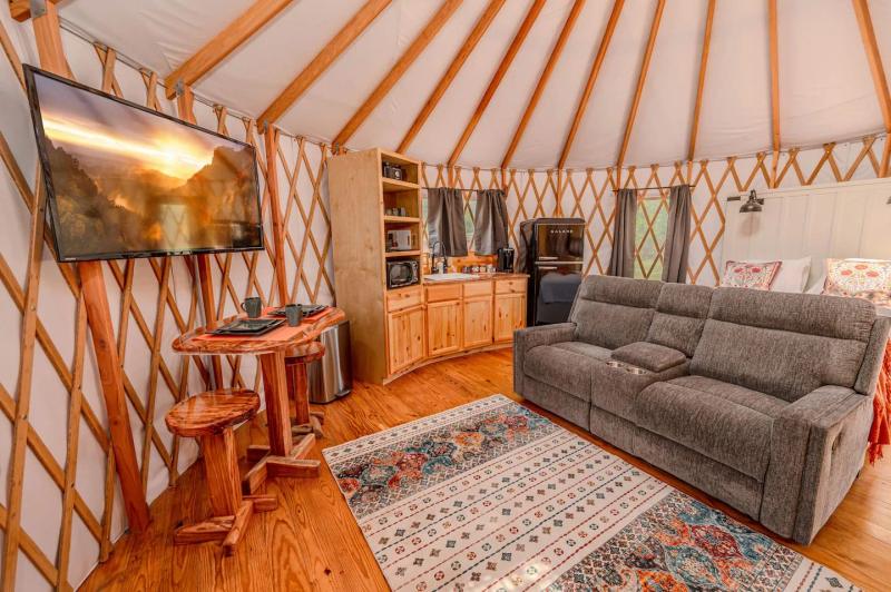 Cockatoo Yurt — living area with loveseat, television, and warm wood cabinetry.