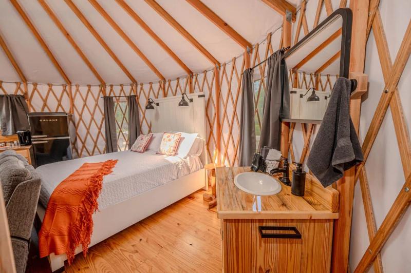Cockatoo Yurt — queen bed dressed with an orange throw beside the wooden vanity and mini fridge.