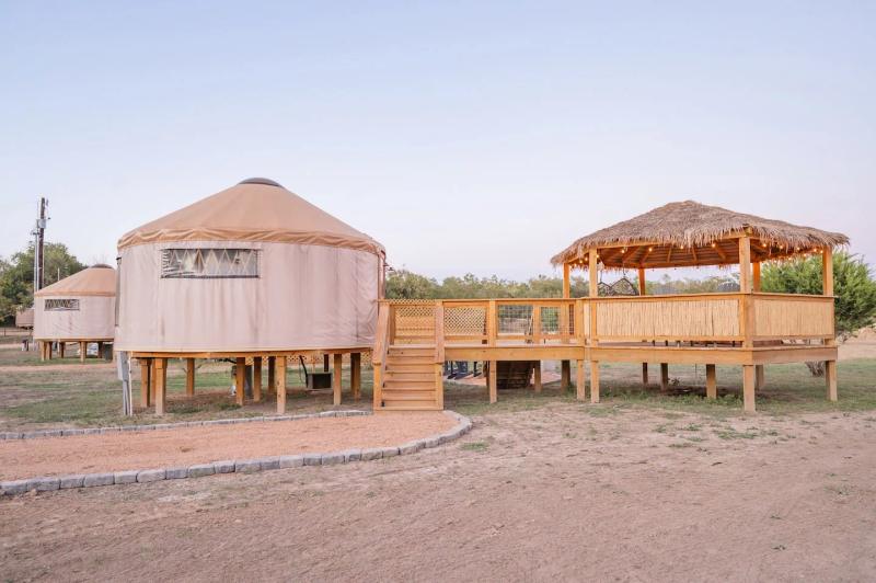 Cockatoo Yurt — canvas yurt raised on cedar posts beside its thatched gazebo at dusk.