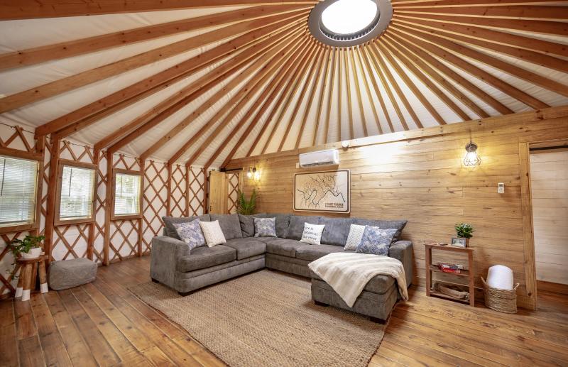Hoot Owl Yurt — grey sectional beneath the roof-beam dome and framed Hill Country river map.