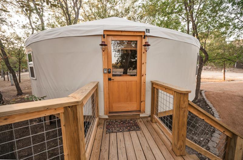 Hoot Owl Yurt — cedar entry deck and glass-paned front door beneath the live oaks.