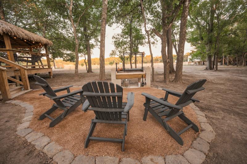 Hoot Owl Yurt — Adirondack chairs arranged around the fire pit under live oaks.