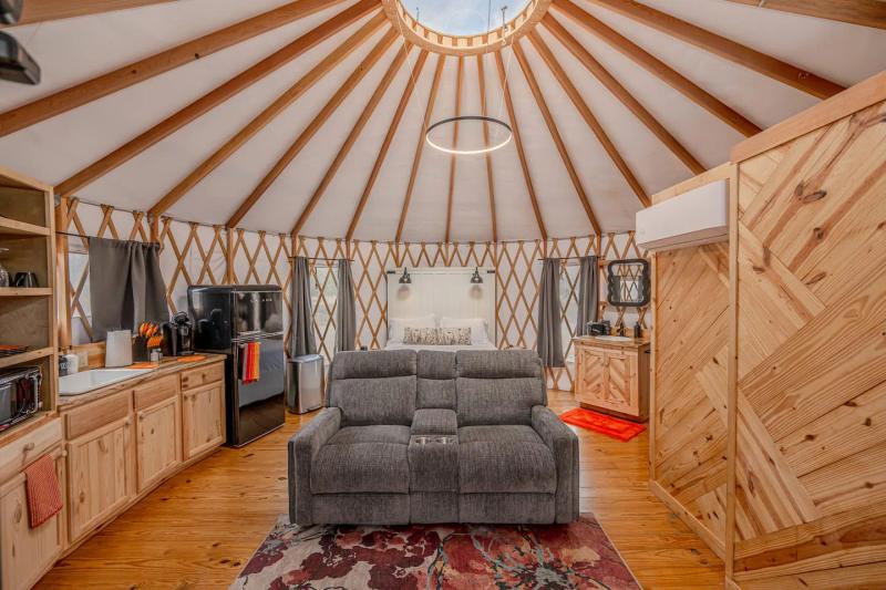 King Fisher Yurt — reclining loveseat, kitchenette and circular ring light under the roof beams.