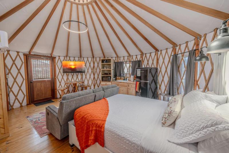 King Fisher Yurt — king bed with an orange throw facing the sunset artwork and kitchenette.