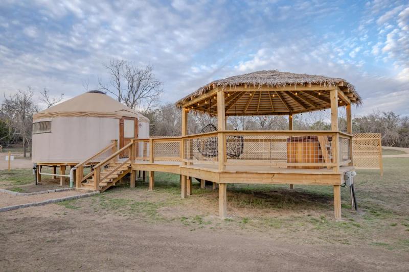 King Fisher Yurt — yurt beside its string-lit thatched gazebo under a cloud-streaked sky.