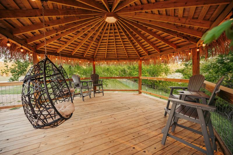 Love Bird Yurt — hanging egg chair and tall Adirondack chairs on the thatched gazebo deck.