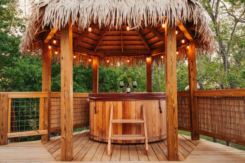 Love Bird Yurt — cedar hot tub set with wine and glasses beneath a string-lit thatched roof.