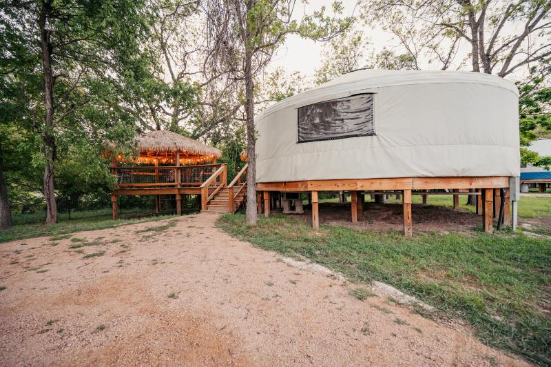 Love Bird Yurt — yurt raised on cedar posts beside the warmly lit gazebo at dusk.