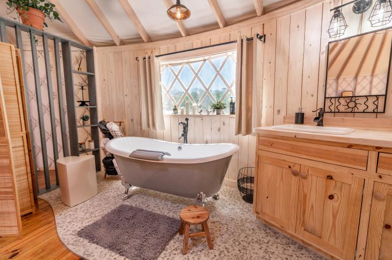 Love Bird Yurt — clawfoot soaking tub beside the pine vanity and lattice window.