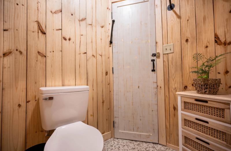Love Bird Yurt — knotty-pine bathroom with pebble-tile floor and a vintage plank door.