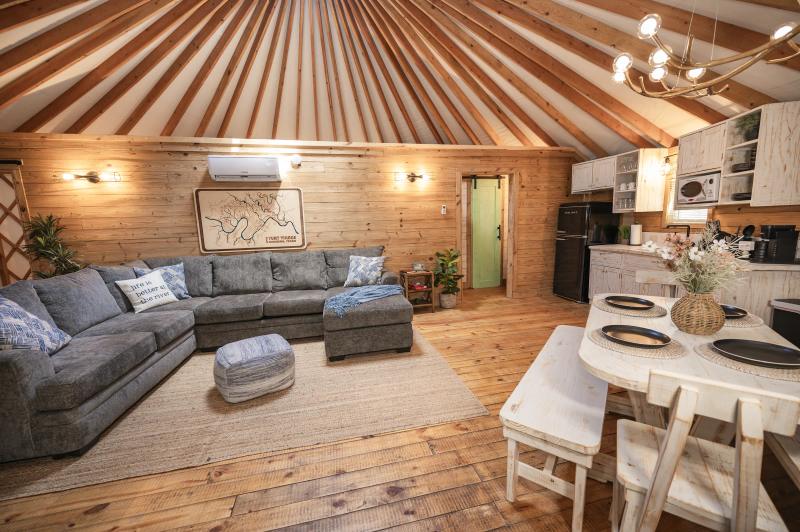 Mockingbird Yurt — grey sectional, branch chandelier and dining table in the open interior.