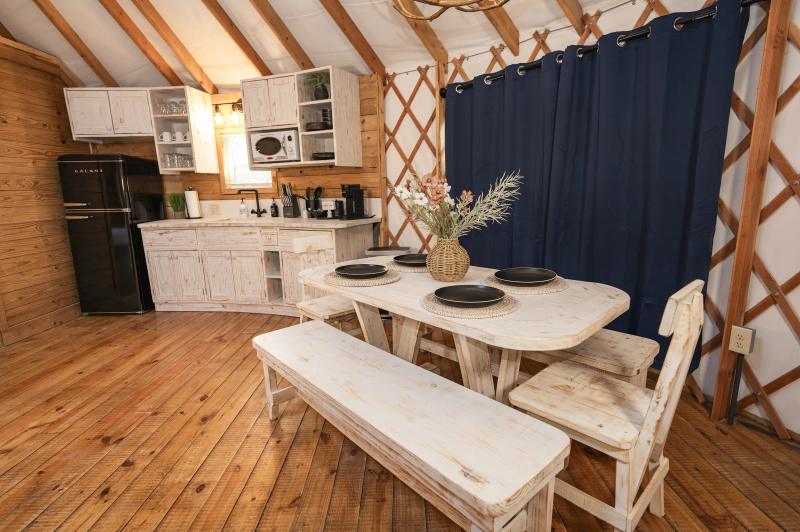 Mockingbird Yurt — whitewashed kitchen with black refrigerator and farm table beside navy curtains.
