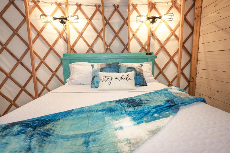 Mockingbird Yurt — queen bed with turquoise linens against the exposed lattice wall.