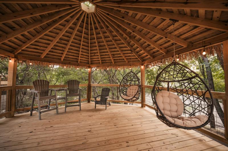 Mockingbird Yurt — cedar gazebo deck with hanging egg chairs and Adirondack chairs among the trees.