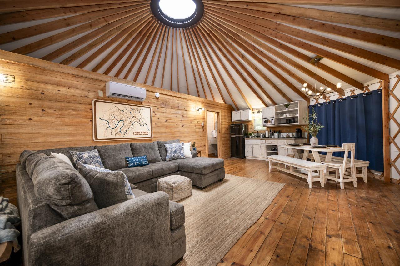 Mourning Dove Yurt — grey sectional, river map art and dining nook beneath the skylight dome.
