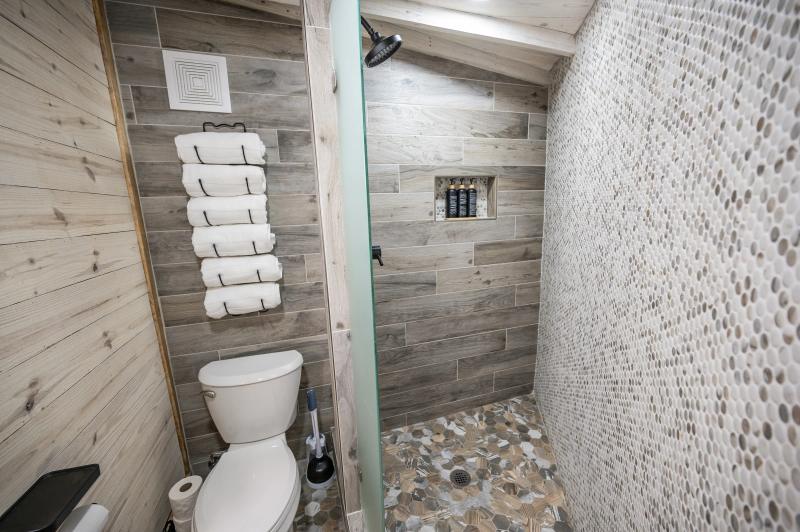 Mourning Dove Yurt — walk-in tiled shower with pebble-stone floor and stacked white towels.