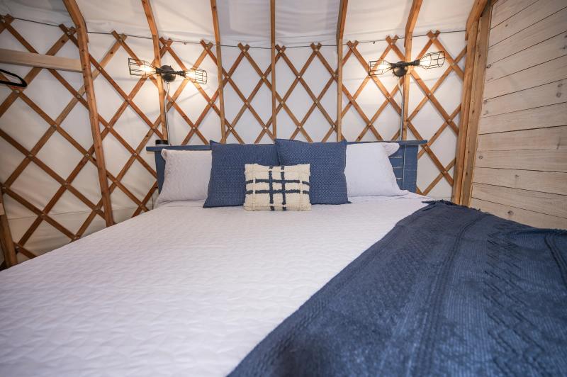 Mourning Dove Yurt — king bed with navy linens against the exposed lattice wall.