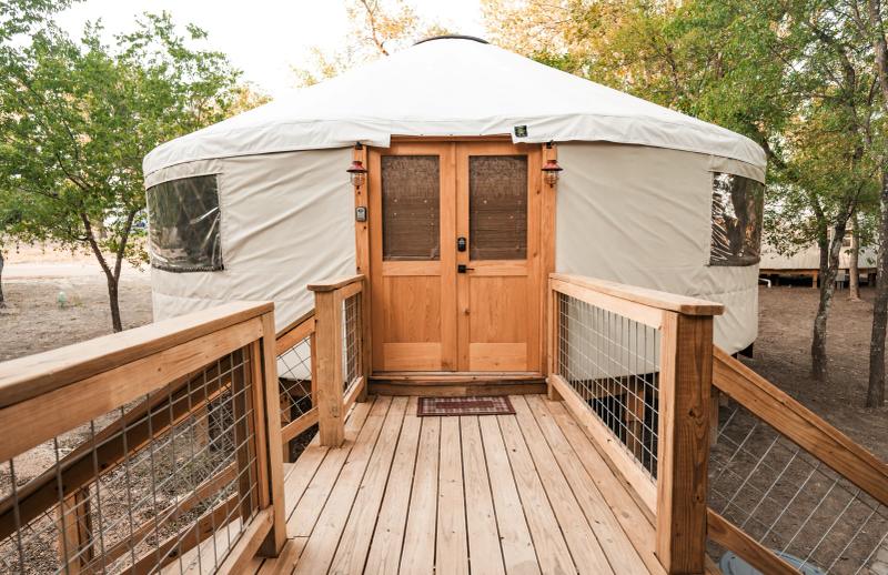 Mourning Dove Yurt — wooden entry deck and double doors beneath mature trees.