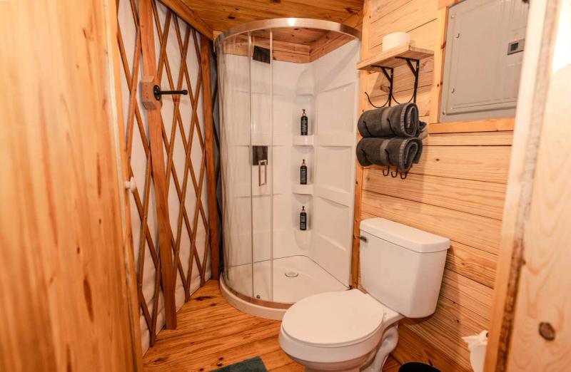 Peacock Yurt — private bathroom with curved glass shower and wood-paneled walls.