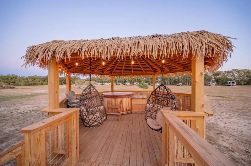 Peacock Yurt — thatched gazebo with hanging chairs and a round cedar hot tub.