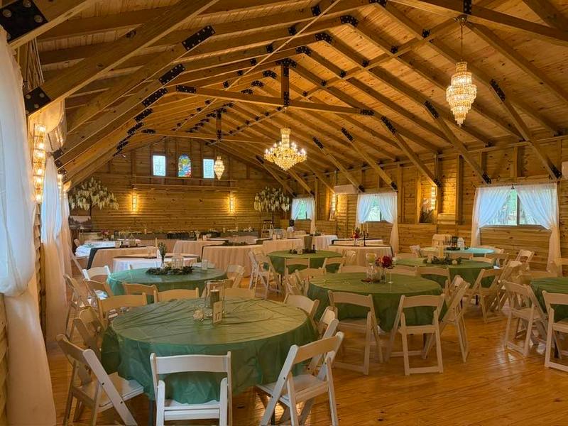 Inside the enclosed, air-conditioned reception hall — round tables in sage linens under chandeliers and warm string lights along the pine walls
