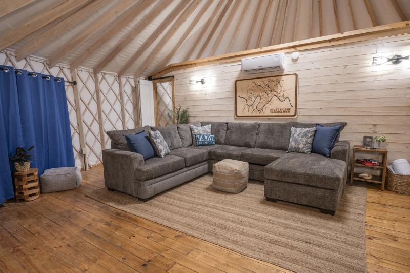 Open yurt living area with a deep sectional, navy drapes and wide plank floors