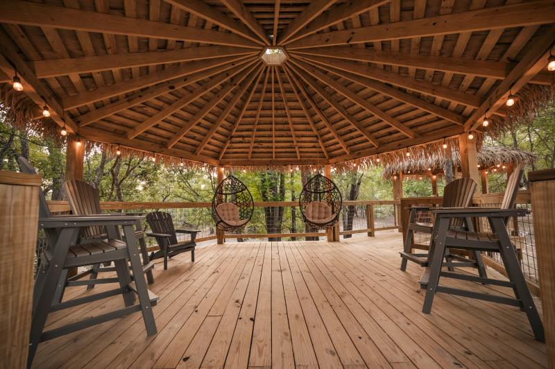 Covered gazebo deck lined with Adirondack chairs and warm string lights at dusk