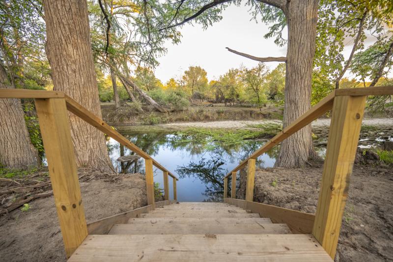 Wooden stairway between two cypress trunks leading down to the Medina River